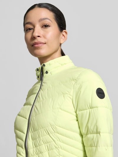 Kobiece modelka ma na sobie Slim Fit Jacke in Stepp-Optik od G.I.G.A. DX w jasnożółtym kolorze, detal z logo, zamek błyskawiczny, wpuszczane kieszenie zapinane na zamek błyskawiczny, odpinany kaptur, pikowany wzór, długość tyłu w rozmiarze 36: 60 cm, szerokość ramion w rozmiarze 36: 45 cm, szerokość klatki piersiowej w rozmiarze 36: 46 cm, długość rękawów w rozmiarze 36: 64 cm, krój slim fit, ujęcie: zbliżenie na górną część ciała z przodu.