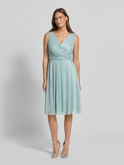 Frauenmodel trägt knielanges Cocktailkleid mit V-Ausschnitt von TROYDEN COLLECTION in schimmerndem Hellblau, tailliert, Ganzkörperansicht von vorne