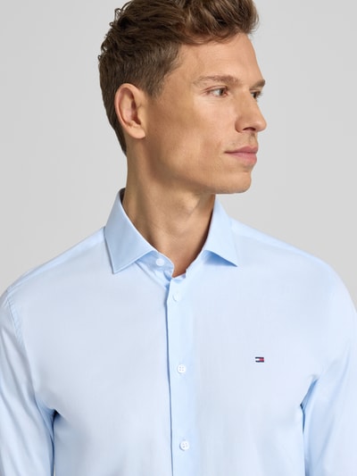 Męski model nosi Slim Fit Businesshemd aus Baumwoll-Mix von Tommy Hilfiger, efekt: jednolity kolor, popelina, kołnierzyk typu kent, wyhaftowane logo, mieszanka bawełny, długi rękaw, na całej długości listwa guzikowa, sportowe mankiety, taliowany krój, jasnoniebieski, zbliżenie na górną część tułowia.