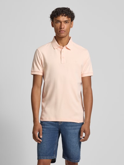 Männermodel trägt Modern Fit Poloshirt mit Logo-Stitching Modell 'Primo' von JOOP! Collection in zartem Pfirsichton, glatte Baumwolltextur, kurze Knopfleiste, Polokragen, kurze Ärmel, Label-Detail, Ganzkörperansicht von vorne.