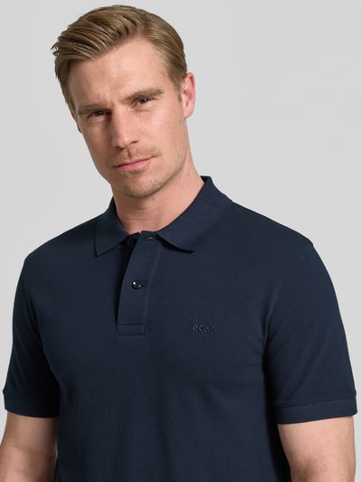 Männermodel trägt Regular Fit Poloshirt aus reiner Baumwolle Modell 'PALLAS' von BOSS in Optik: Unifarben mit Label-Stitching-Applikation, Polokragen, kurzer Knopfleiste, Kurzarm und Piqué-Materialverarbeitung, Nahaufnahme Oberkörper.