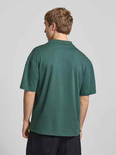 Męski model nosi Boxy Fit Poloshirt aus Baumwoll-Mix Modell 'CASPIAN AIRLEX' od Only & Sons, zielony jersey, krótki rękaw, gładki, label patch, całkowity widok z tyłu.