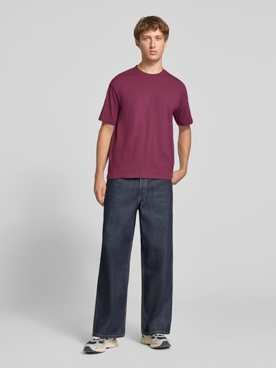 Männermodel trägt Relaxed Fit T-Shirt aus reiner Baumwolle von Marc O'Polo DENIM in Weinrot zu dunkler Jeans, Ganzkörperansicht von vorne.