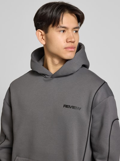 Männermodel trägt Hoodie mit Logo und Känguru-Tasche von REVIEW in Grau, Baumwoll-Mix, Regular-Fit, Nahaufnahme Oberkörper.
