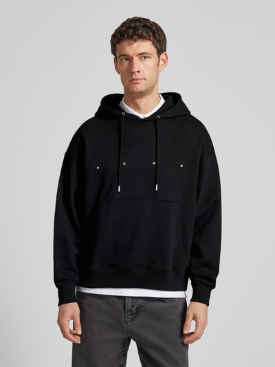 Männermodel trägt Relaxed Fit Hoodie aus reiner Baumwolle Modell 'DOLAND' von HUGO, schwarz, unifarben, Label-Schriftzug, Sweat-Material, Ganzkörperansicht von vorne.