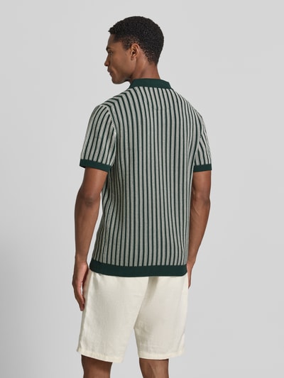 Męski model nosi Regular Fit Poloshirt in Strick-Optik od MCNEAL z bawełny, krój regular fit, kołnierzyk polo, krótki rękaw, imitacja dzianiny, długość tyłu 71 cm, długość rękawów 24 cm, pionowe paski, ciemnozielone i kremowe kolory, faktura dzianiny, widok całej sylwetki od tyłu.