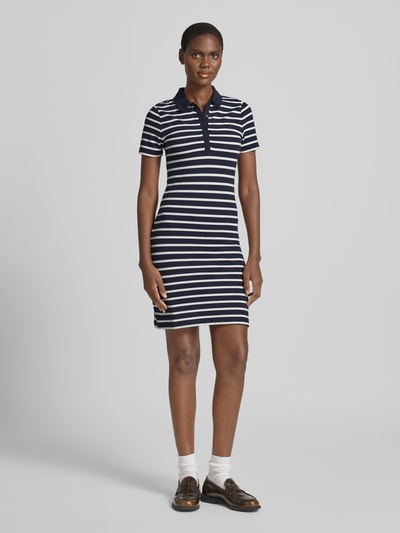 Vrouwenmodel draagt Knielanges Polokleid mit kurzer Knopfleiste van Gant, donkerblauw-wit gestreept, katoenmix met stretch, aansluitende fit, knielang, polokraag, korte knoopsluiting, ruglengte maat S 88 cm, borstwijdte 42 cm, mouwlengte 19 cm, full body van voren.