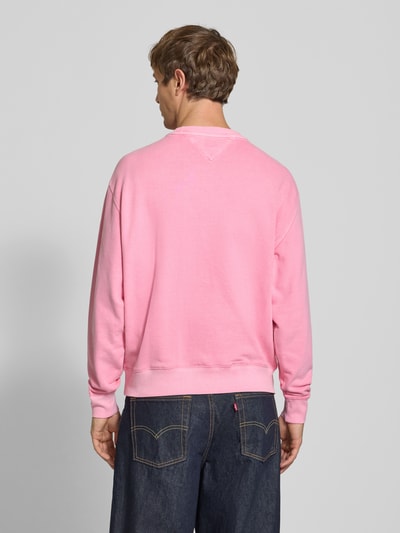 Männermodel trägt Relaxed Fit Sweatshirt aus reiner Baumwolle von Tommy Jeans in Rosa, glatte Textur, Ganzkörperansicht Rückansicht. Herren Sweatshirt von Tommy Jeans