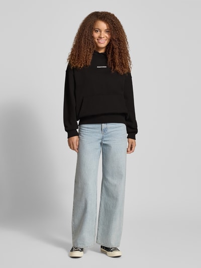 Vrouwenmodel draagt Oversized Hoodie met Label-Stitching model 'CLARITA' van Pegador, katoenmix, zwart, oversized fit, voorkant volledige lichaamsweergave.
