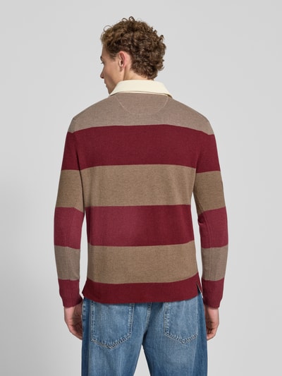 Männermodel trägt Regular Fit Pullover aus reiner Baumwolle von GANT in Rot und Braun mit breiten Streifen, Ganzkörperansicht Rückansicht.