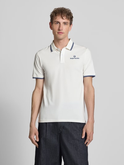 Männermodel trägt Slim Fit Poloshirt mit Logo-Stitching Modell 'Reed' von SERGIO TACCHINI, weiß mit blauen Details, Ganzkörperansicht von vorne. Elastischer Baumwoll-Mix, kurzärmeliges Design, Polokragen, Rückenlänge bei Größe M: 71 cm.