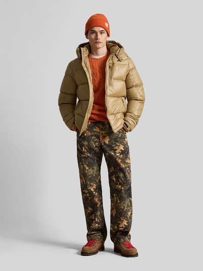 Männermodel trägt Regular Fit Steppjacke mit Zweiwege-Reißverschluss von Polo Ralph Lauren in Beige mit glatter Oberfläche, Ganzkörperansicht von vorne. Herren Steppjacke von Polo Ralph Lauren