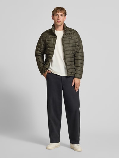 Männermodel trägt Jacke mit Label-Patch Modell 'ELVIS' von JACK & JONES in Oliv, Stehkragen, Reißverschlüssen, Ganzkörperansicht von vorne.