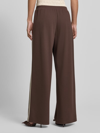 Frauenmodel trägt Jog Pants mit französischen Eingrifftaschen von Jake*s Casual in Braun, Wide-Leg-Fit, Material-Mix mit Stretch-Anteil, elastischer Bund, Ganzkörperansicht Rückansicht.