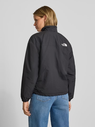 Frauenmodel trägt Jacke mit Wendefunktion Modell 'YUMIORI' von The North Face in Schwarz, glatte Textur, Ganzkörperansicht Rückansicht, Regular Fit, Stehkragen, Logo und Wendefunktion, Rückenlänge 62 cm, Schulterbreite 52 cm, Brustweite 57 cm, Ärmellänge 57 cm.