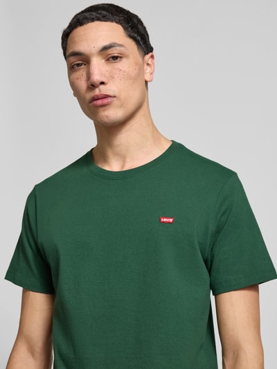 Męski model nosi Regular Fit T-Shirt aus reiner Baumwolle od Levi’s®, zielony, krój regular fit, patch z logo, detaliczny splot, unikatowa struktura, jednolity kolor, materiał bawełniany, półokrągły dekolt, krótki rękaw, Nahaufnahme górnej części ciała.