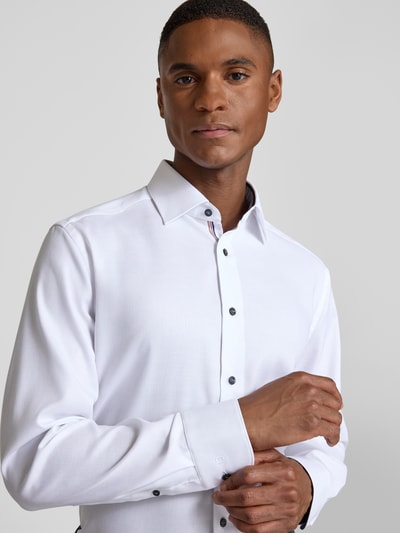 Männermodel trägt Regular Fit Businesshemd aus reiner Baumwolle mit Kentkragen von OLYMP, weiß mit schwarzen Knöpfen, Nahaufnahme Oberkörper, durchgängige Knopfleiste, Sportmanschetten.