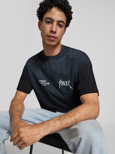 Männermodel trägt schwarzes T-Shirt mit weißem Statement-Print, Baumwolle, Boxy Fit, SRC® Pacer von ANOTHER COTTON LAB, Nahaufnahme Oberkörper