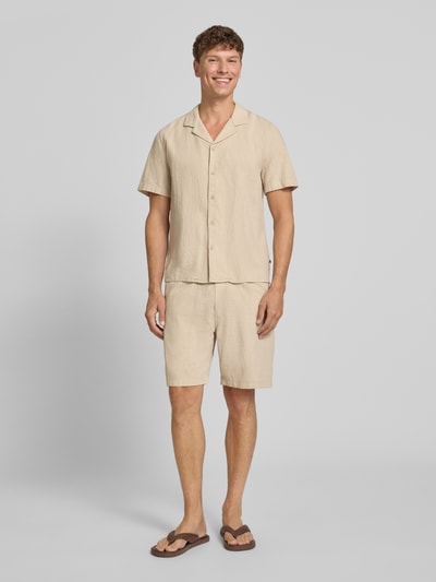 Männermodel trägt Relaxed Fit Stoffshorts aus einer Baumwolle von s.Oliver RED LABEL in Beige, lockere Struktur, Ganzkörperansicht von vorne.