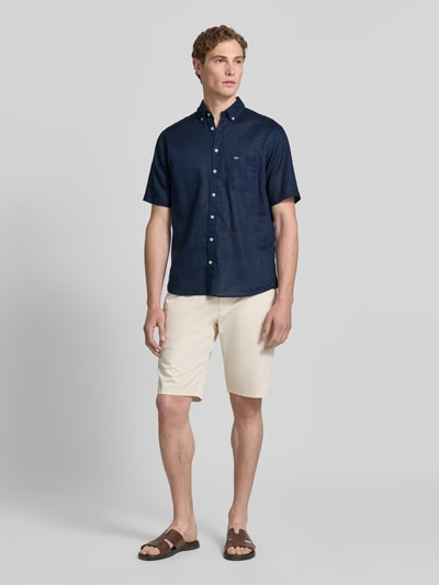 Männermodel trägt Slim Fit Freizeithemd aus Leinen-Baumwoll-Mix von Fynch-Hatton in Dunkelblau, Button-Down-Kragen, Brusttasche, Label-Stitching, Knopfleiste, Kombi mit heller Shorts, Ganzkörperansicht von vorne. Rückenlänge bei Größe M: 74 cm, Schulterbreite: 48 cm, Ärmellänge: 26 cm.