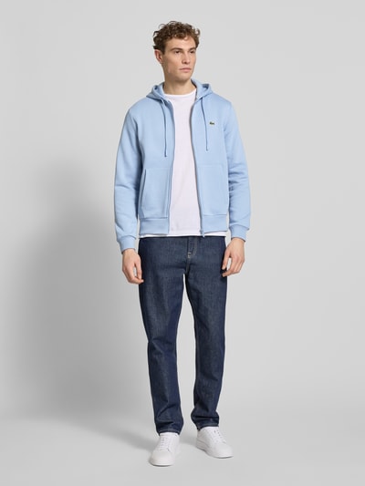 Męski model nosi Regular Fit Sweatjacke aus Baumwoll-Mix od Lacoste, jasnoniebieska, kieszenie z przodu, logo, bawełniany mix, krój regular fit, zamek, kaptur, przód, widok całej sylwetki