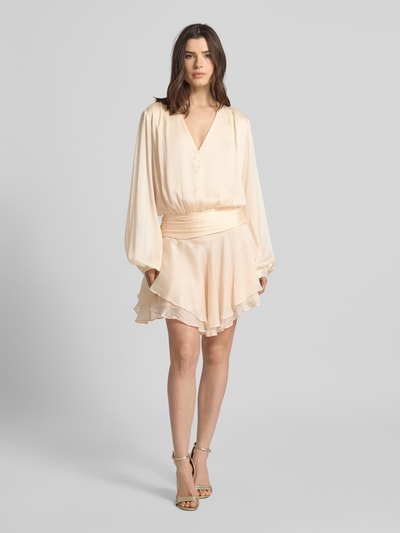 Frauenmodel trägt Minikleid mit kurzer Knopfleiste Modell 'MAGALI' von Guess, Taillierter Schnitt, V-Ausschnitt, Volantsaum, Cremefarben, Ganzkörperansicht von vorne.