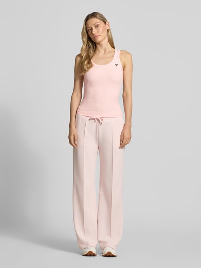 Kobiece modelka nosi Slim Fit Top aus Viskose-Mix Modell 'Colette' od Guess Activewear, elastyczna różowa tkanina, krój slim fit, logo na piersi, okrągły dekolt, długość pleców w rozmiarze S: 51 cm, pełny widok z przodu.
