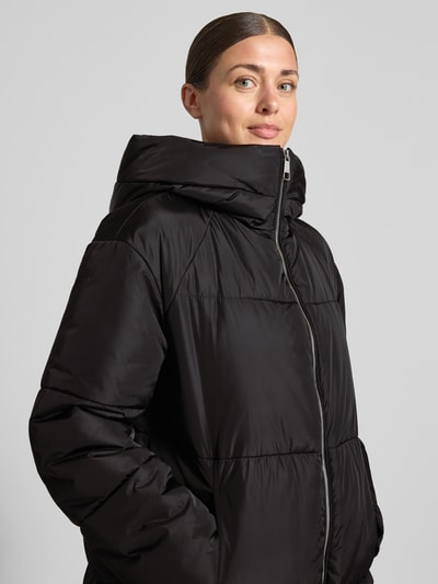 Frauenmodel trägt Daunenmantel mit Kapuze Modell 'C_Polliana' von BOSS Orange in Schwarz, unifarben, zweiwege-Reißverschluss, glänzende Oberfläche, Nahaufnahme Oberkörper.