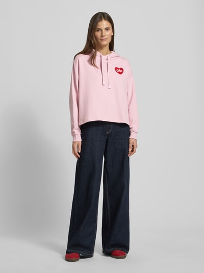 Frauenmodel trägt Hoodie mit Kapuze von Oui in Rosa aus Baumwoll-Mix mit Lockerer-Schnitt, Kapuze, Tunnelzug, Label-Detail, gerippte Ärmelabschlüsse, Ganzkörperansicht von vorne.