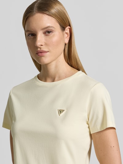 Kobiece modelka nosi Regular Fit T-Shirt mit Logo-Applikation Modell 'Colette' od Guess Activewear, elastyczna bawełna, krój regular fit, kremowy kolor, logo na piersi, okrągły dekolt, długość pleców w rozmiarze S: 60 cm, zbliżenie na górną część ciała z przodu