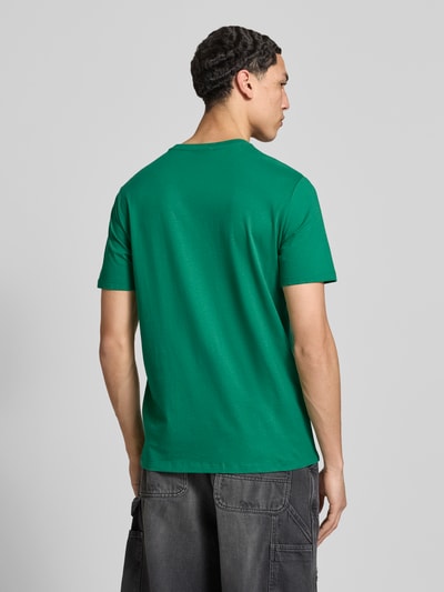 Männermodel trägt T-Shirt mit Label-Badge von Calvin Klein Jeans in Grün, reine Baumwolle, Regular Fit, Rückansicht, Ganzkörperansicht.