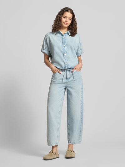 Frauenmodel trägt Relaxed Fit Kurzarmbluse aus reiner Baumwolle von Marc O'Polo Denim, Denim-Optik, Hemdblusenkragen, Knopfleiste, kurzarm, hellblaue Farbtöne, glatte Textur, Ganzkörperansicht von vorne.