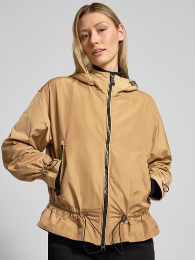 Modelka nosi Kurtka 'Jacke mit Zweiwege-Reißverschluss' von Fuchs Schmitt, krój regular fit, kaptur z tunelem, zamek błyskawiczny dwustronny, kieszenie zapinane na zamek błyskawiczny, długość tyłu w rozmiarze 36: 67 cm, szerokość ramion w rozmiarze 36: 53 cm, szerokość klatki piersiowej w rozmiarze 36: 59 cm, długość rękawów w rozmiarze 36: 57 cm, beżowy, lekko matowa tekstura, prosty krój, całkowity widok z przodu.