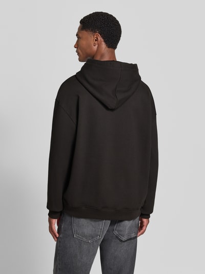 Männermodel trägt Regular Fit Hoodie aus reiner Baumwolle Modell 'Diflowhood' von HUGO in Schwarz, lockere Passform, Ganzkörperansicht Rückansicht. Herren Hoodie von HUGO