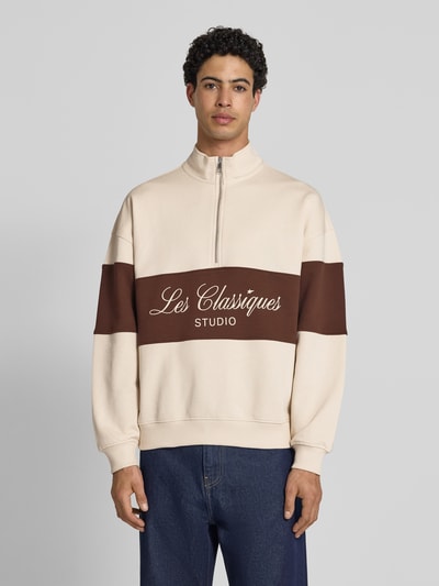 Männermodel trägt Oversized Troyer aus reiner Baumwolle Modell 'LES CLASSIQUES' von Only & Sons in Two-Tone-Optik, Schriftzug, Label-Patch, Troyer-Kragen, kurzer Reißverschluss, Langarm, Sweat, Passform: oversized, Rumpfabschluss und Ärmelabschluss gerippt, Materialverarbeitung: Sweat, Ganzkörperansicht von vorne.