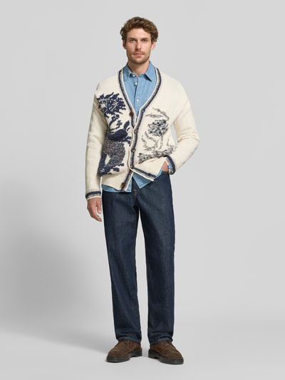 Männermodel trägt Strickjacke mit V-Ausschnitt Modell 'INTARSIA' von Scotch & Soda, creme mit dunkelblauem Allover-Look, Baumwoll-Mix, Knopfleiste, Regular Fit, Ganzkörperansicht von vorne.