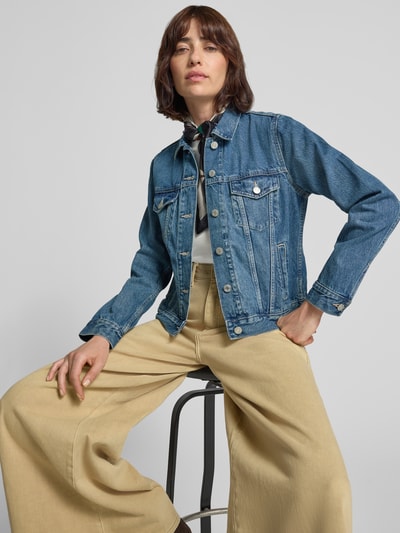 Frauenmodel trägt Jeansjacke mit Brusttaschen von GAP in Mittelblau, reine Baumwolle, Regular Fit, Ganzkörperansicht von vorne.