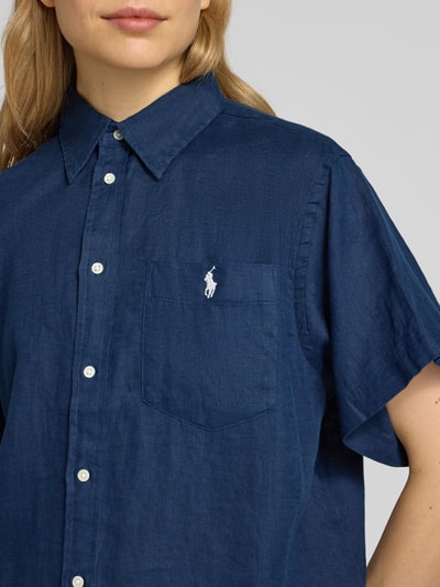 Frauenmodel trägt Oversized Hemdbluse aus reinem Leinen von Polo Ralph Lauren in Dunkelblau mit Logo-Stitching, Nahaufnahme Oberkörper.