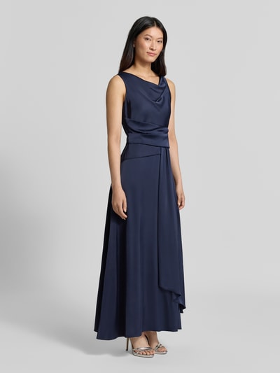 Frauenmodel trägt Abendkleid mit Wasserfallausschnitt von Rinascimento in Dunkelblau, fließender Stoff, Material-Mix mit Stretch-Anteil, taillierte Passform, Raffungen, Stoffgürtel, rückseitiger Reißverschluss, Ganzkörperansicht von vorne.