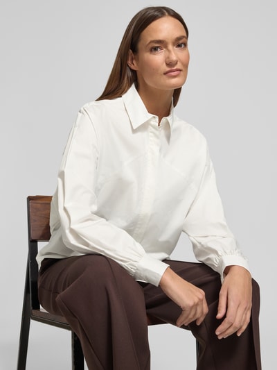 Frauenmodel trägt Regular Fit Hemdbluse mit Hemdblusenkragen von Fynch-Hatton aus reiner Baumwolle, Logo-Applikation, langärmelig, Sportmanschetten, weiße glatte Textur, kombiniert mit brauner Hose, Nahaufnahme Oberkörper.
