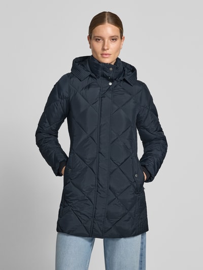 Frauenmodel trägt Regular Fit Mantel in Stepp-Optik von FUCHS SCHMITT in Dunkelblau, Kapuze mit Stehkragen, Eingrifftaschen, Ganzkörperansicht von vorne. Rückenlänge 84 cm, Schulterbreite 42 cm, Brustweite 47 cm, Ärmellänge 64 cm.