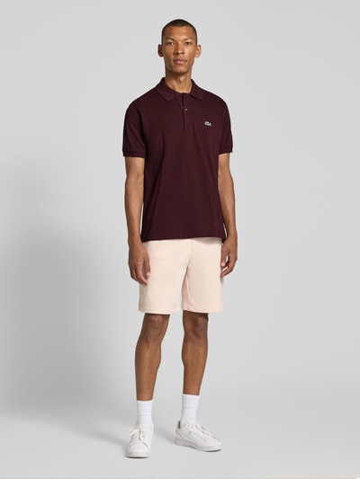 Männermodel trägt Regular Fit Shorts aus Baumwoll-Mix von Lacoste in hellem Beige und Polo in Dunkelrot, Ganzkörperansicht von vorne. Herren Sweatshorts von Lacoste.