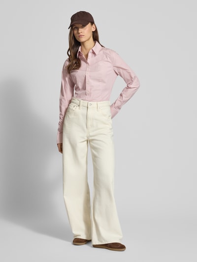 Frauenmodel trägt Slim Fit Hemdbluse aus reiner Baumwolle von Guess Jeans in Rosa, kombiniert mit weißer weiter Hose, Ganzkörperansicht von vorne. Bluse tailliert mit Hemdblusenkragen, durchgehender Knopfleiste und Sportmanschetten, geeignet für einen sportlich-eleganten Look.