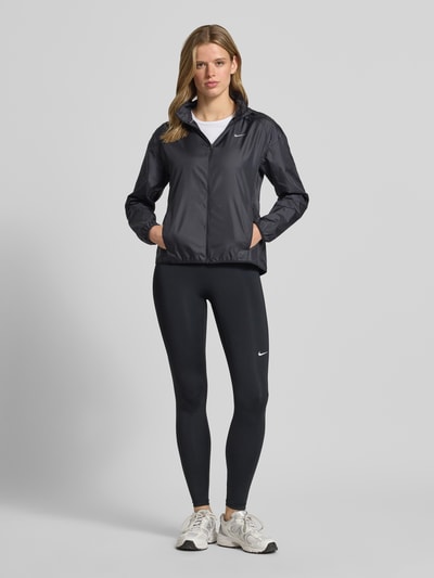 Frauenmodel trägt schwarze Trainingsjacke mit Logo-Print Modell 'Tempo' von NIKE TRAINING, Gerader-Schnitt, Kapuze mit Kordelzug, Reißverschluss, seitliche Eingrifftaschen, glatte Textur, Ganzkörperansicht von vorne.
