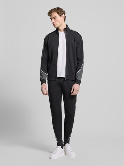 Männermodel trägt Regular Fit Sweatpants aus Baumwoll-Mix von BOSS in Optik: Unifarben mit Galonstreifen, Label-Applikation aus Metall, Ganzkörperansicht von vorne