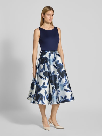 Frauenmodel trägt Cocktailkleid mit Rundhalsausschnitt von SWING aus Satin in A-Linie, Midikleid mit floralem Muster, Ganzkörperansicht von vorne. Rückenlänge bei Größe 36: 113 cm, Brustweite bei Größe 36: 34 cm, rückseitiger Reißverschluss.