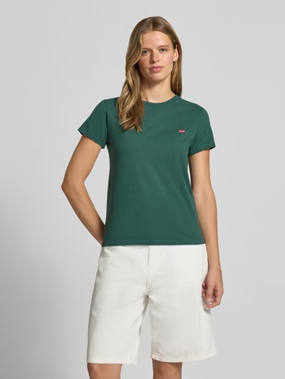 Frauenmodel trägt Regular Fit T-Shirt aus reiner Baumwolle von Levi's® in Dunkelgrün, kombiniert mit weißen Shorts, Ganzkörperansicht von vorne.