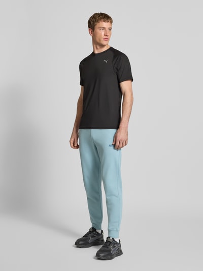 Männermodel trägt T-Shirt mit Label-Print von PUMA PERFORMANCE, schwarzer Material-Mix mit Stretch-Anteil, Regular Fit, ganzkörperansicht von vorne.
