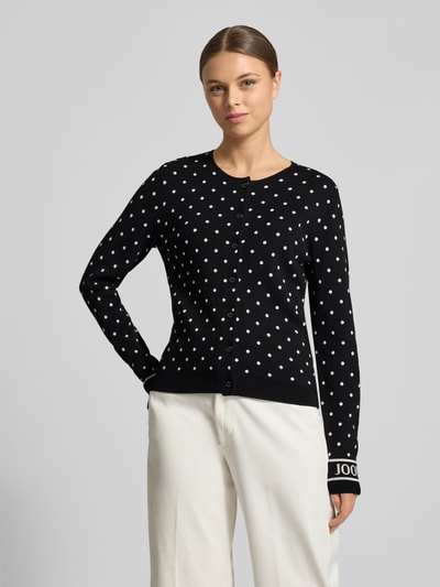 Frauenmodel trägt Regular Fit Cardigan aus Viskose-Mix Modell 'Karli' von JOOP! in Strick-Optik mit Rundhalsausschnitt, durchgängiger Knopfleiste, Logo-Stitching, schwarz mit weißen Punkten, Damen Cardigan, Ganzkörperansicht von vorne.