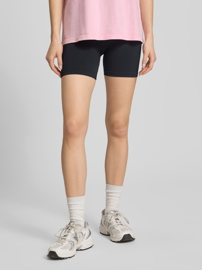 Frauenmodel trägt Slim Fit Shorts mit Logo-Print Modell 'Restore' von P.E Nation in Schwarz, Elastischer-Material-Mix, breiter Bund, Ganzkörperansicht von vorne.